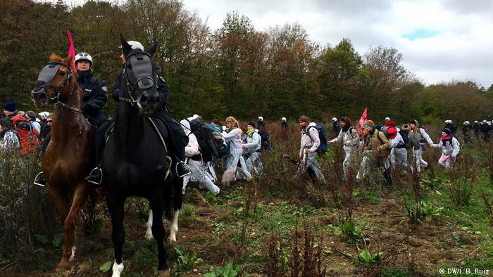 Protesters approach the forest during a massive anti-coal protest in western Germany. Two police officers on horseback watch and many police officers on foot follow protesters